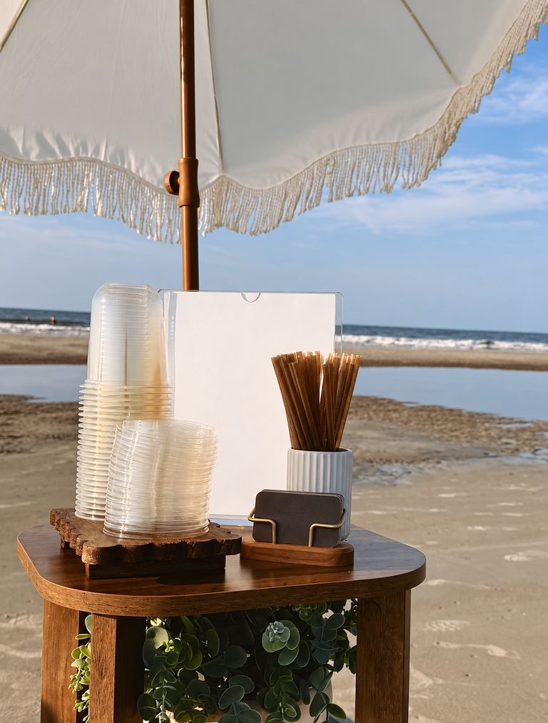Stacked cups, a blank menu card and a cup of wooden stirrers on a wooden service table at a beach pop-up